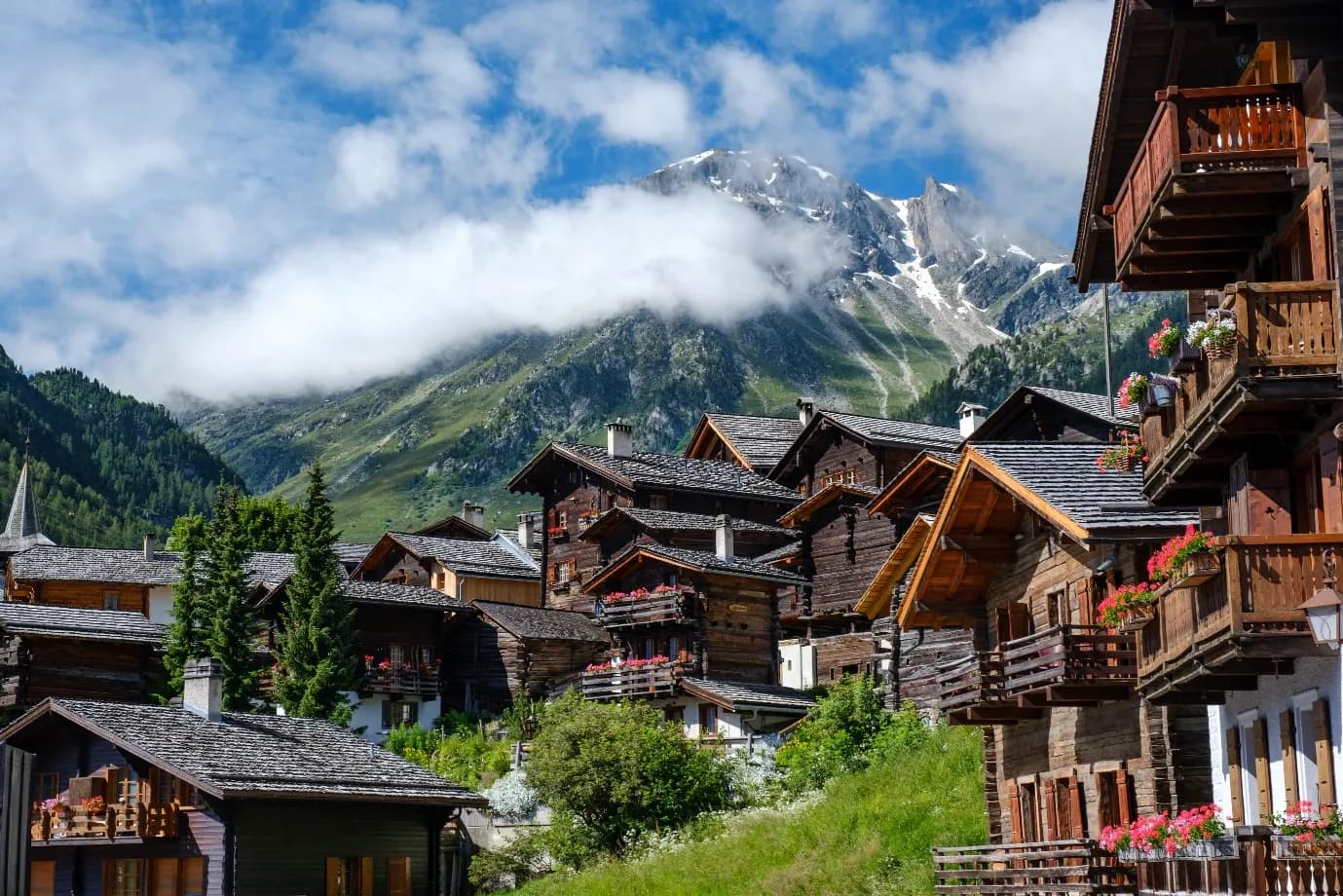 Timber alpine chalets below a cloud-wrapped mountain